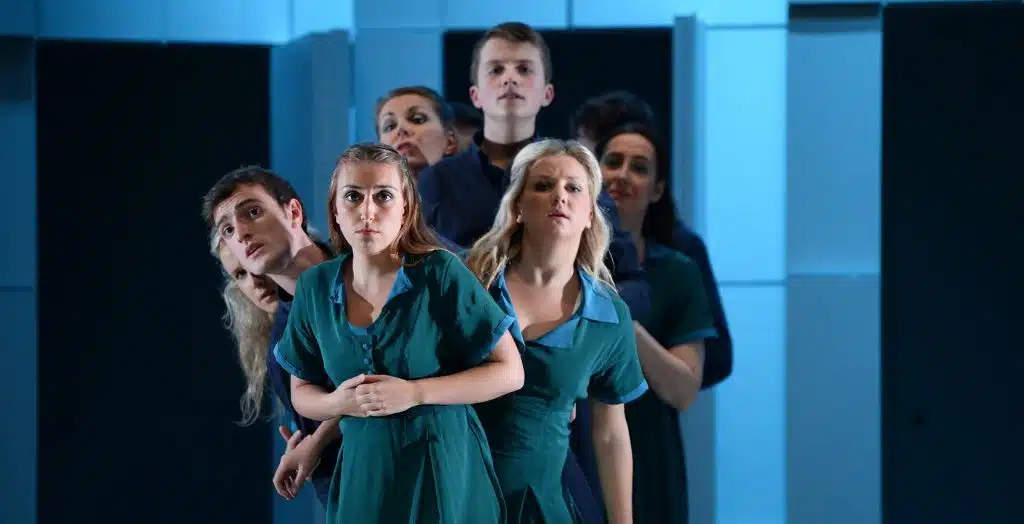 A group in teal uniforms stand on stage, ready for Siamsa Tíre traditional Irish arts performances.