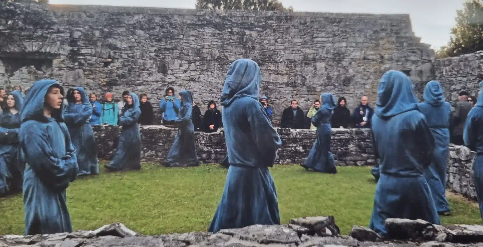 People in blue hooded robes gather at Arts centre Tralee Kerry, watched by onlookers.