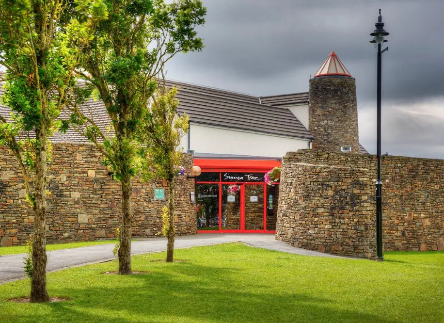 A stone building with red doors near the Arts centre Tralee Kerry, set among trees and grass.
