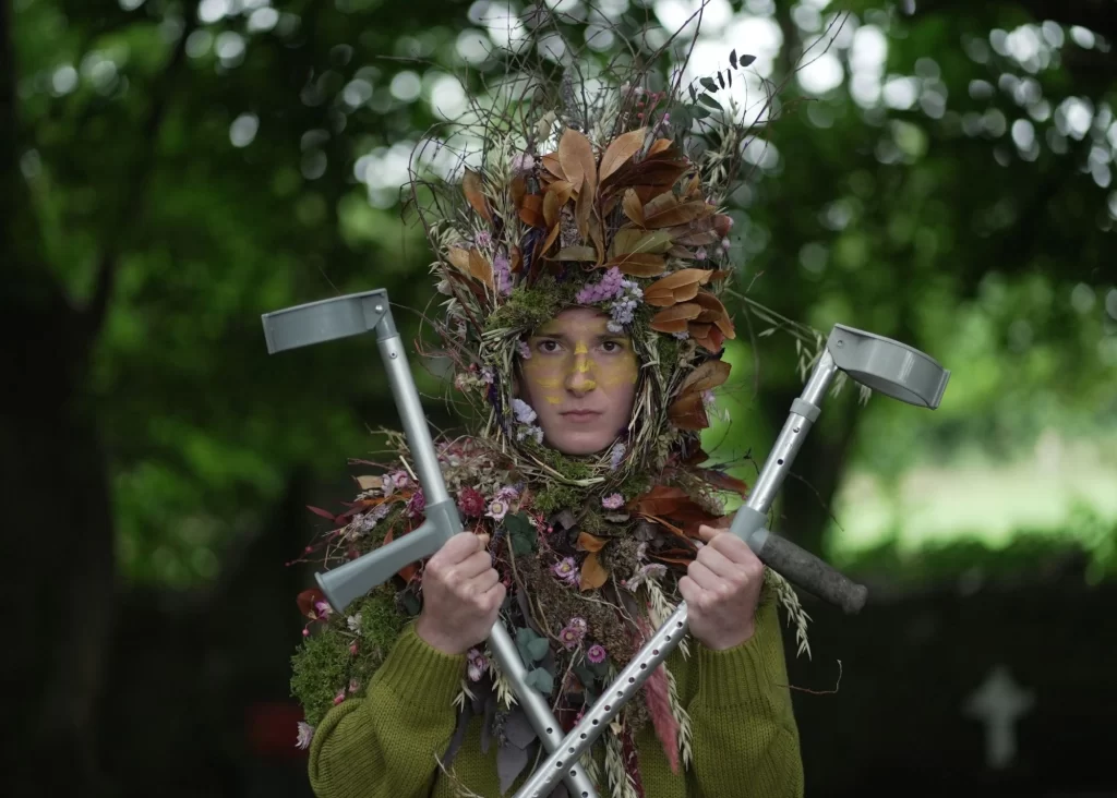 Person in leafy, floral costume with crutches stands outdoors at Siamsa Tíre theatre Tralee.