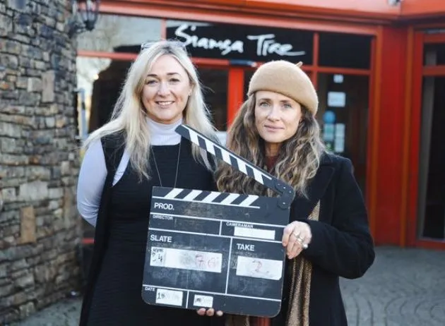 Two women hold a clapperboard outside the Siamsa Tíre theatre Tralee building.