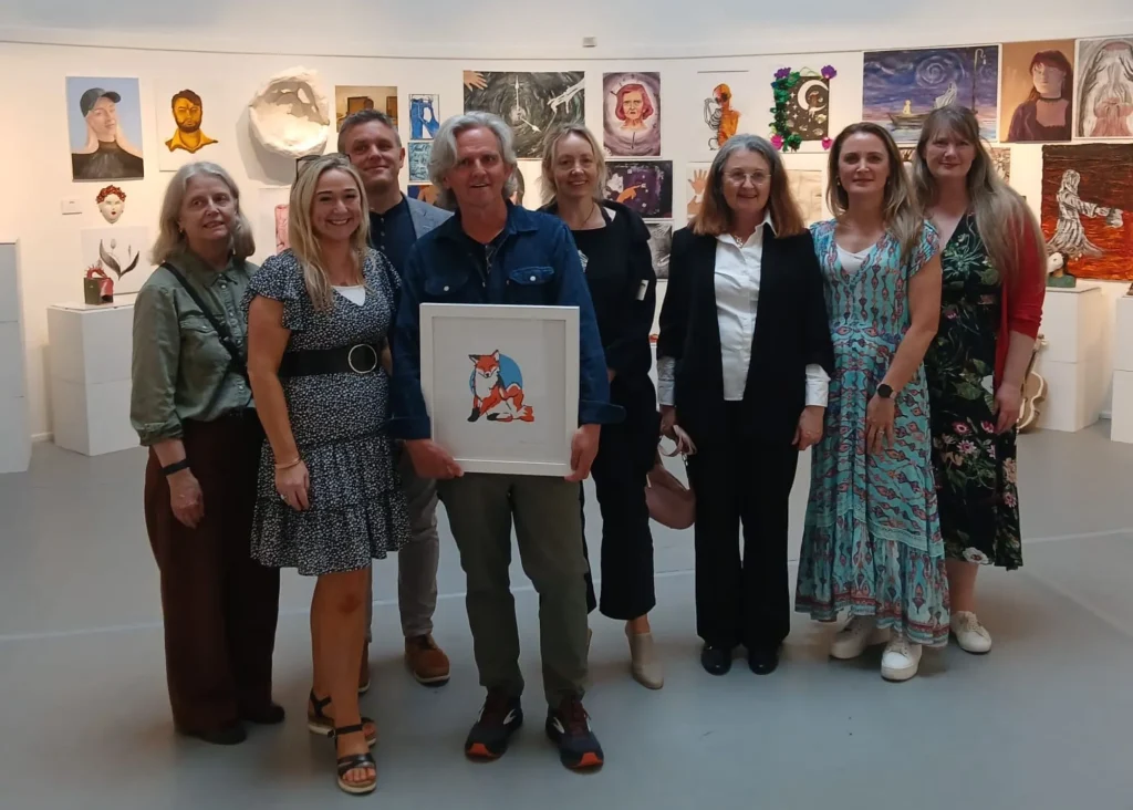 Eight people pose at Siamsa Tíre theatre Tralee; the man in front holds a framed fox illustration.