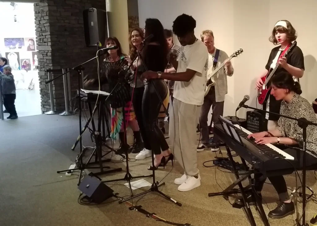 A band performs indoors at Siamsa Tíre theatre Tralee with vocals, guitar, keyboard, and bass.