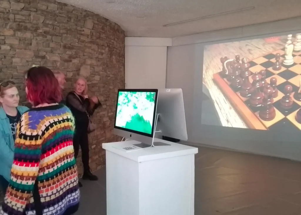 People view screens and a chessboard at Siamsa Tíre theatre Tralee with a stone wall backdrop.