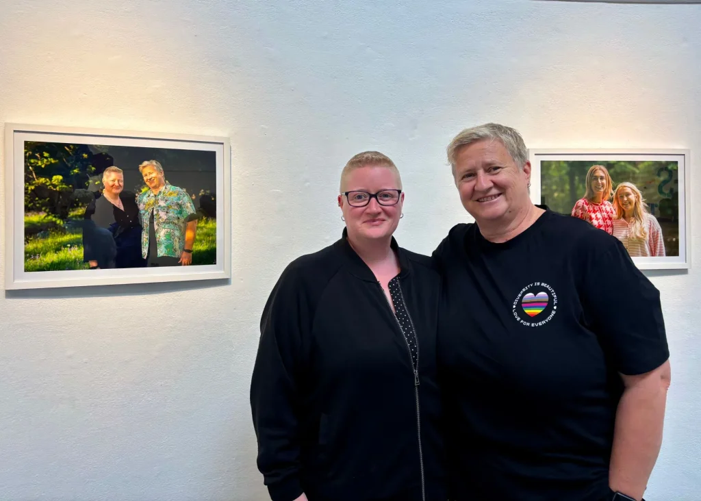 Two people smiling at Siamsa Tíre theatre Tralee, framed photos on a white gallery wall.