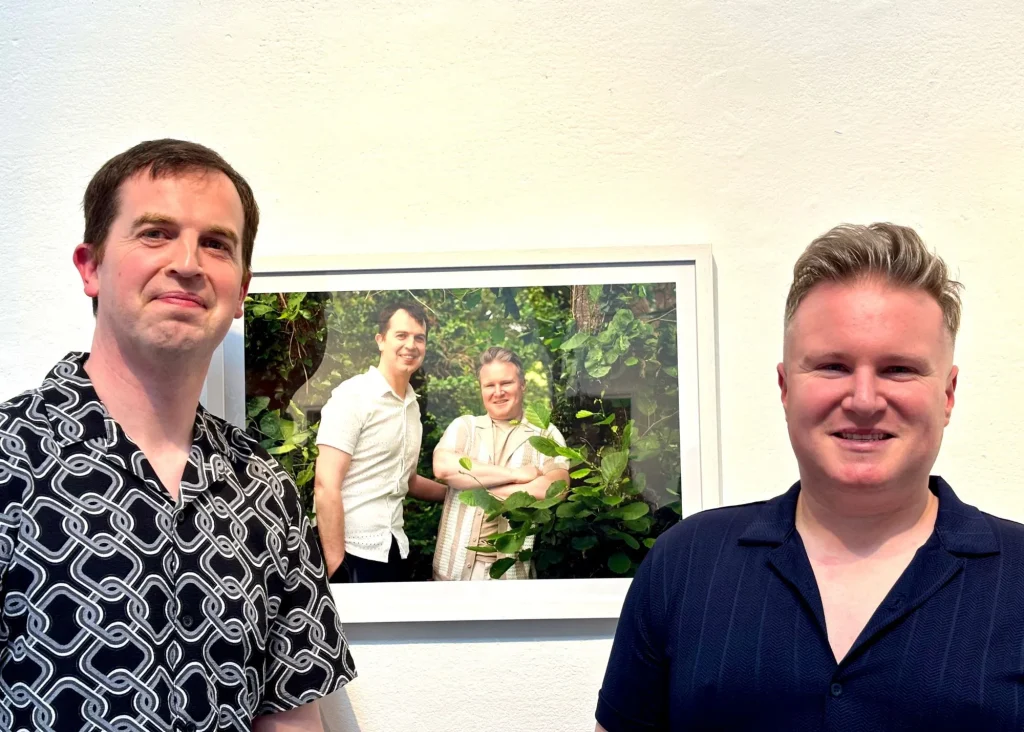 Two men smile before their photo at Siamsa Tíre theatre Tralee with greenery in the background.