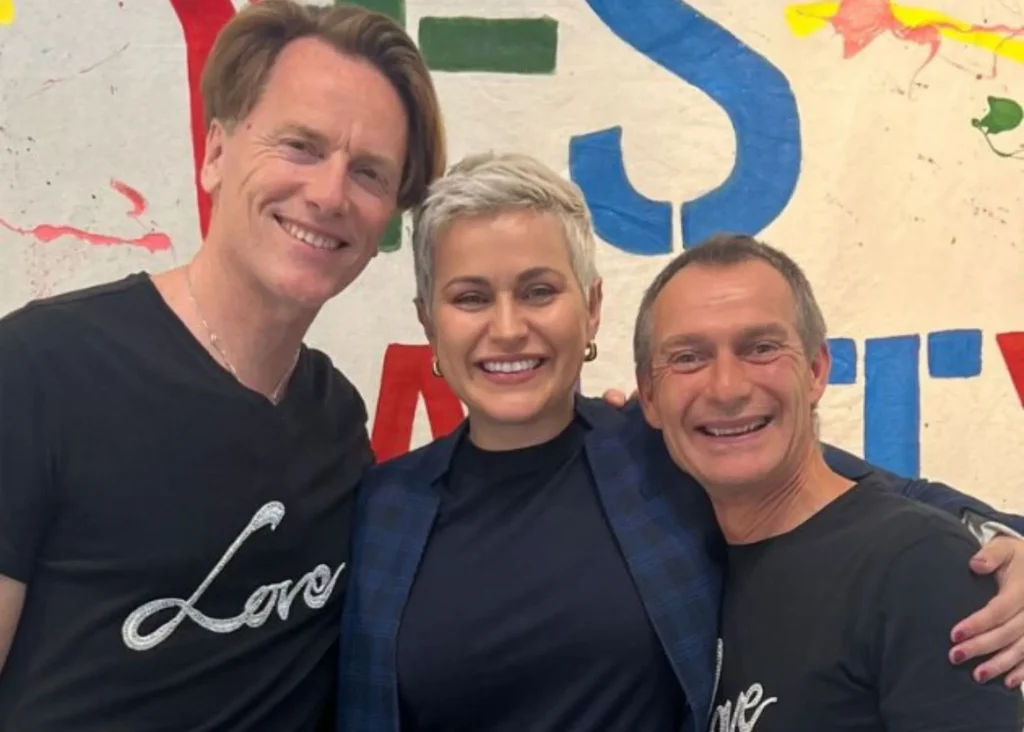 Three people smiling together at Siamsa Tíre, arts centre in Tralee, with paint splatters behind.