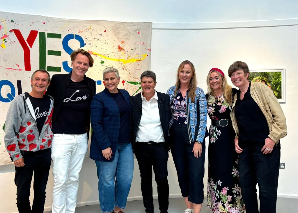 Seven people smiling in front of a colorful "YES QUEER" banner at Siamsa Tíre theatre Tralee.