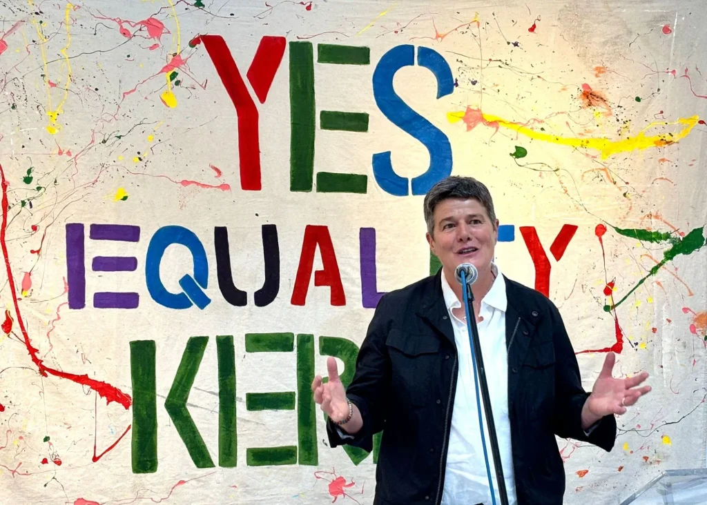Person speaks before a colorful "YES EQUALITY" banner at Siamsa Tíre theatre Tralee.