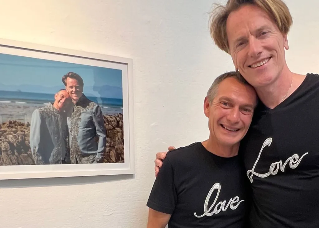 Two smiling men in "love" shirts hug by a photo at the Siamsa Tíre venue hire Tralee.