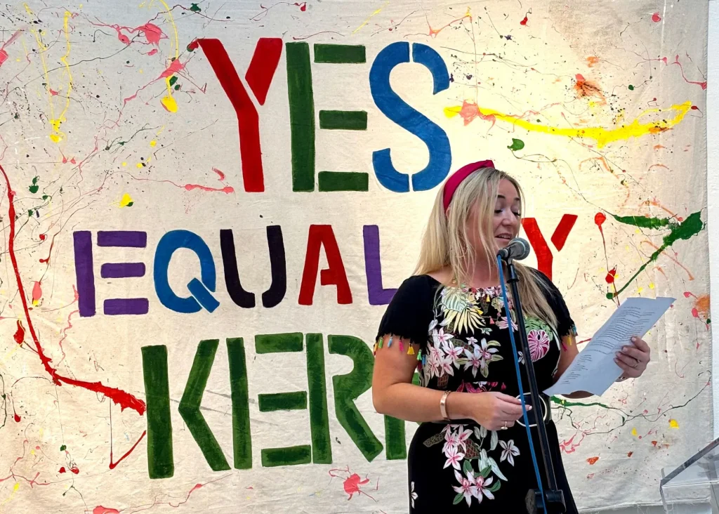 Woman speaks at a podium before a vibrant "YES EQUALITY KIERAN" banner at Siamsa Tíre Tralee.