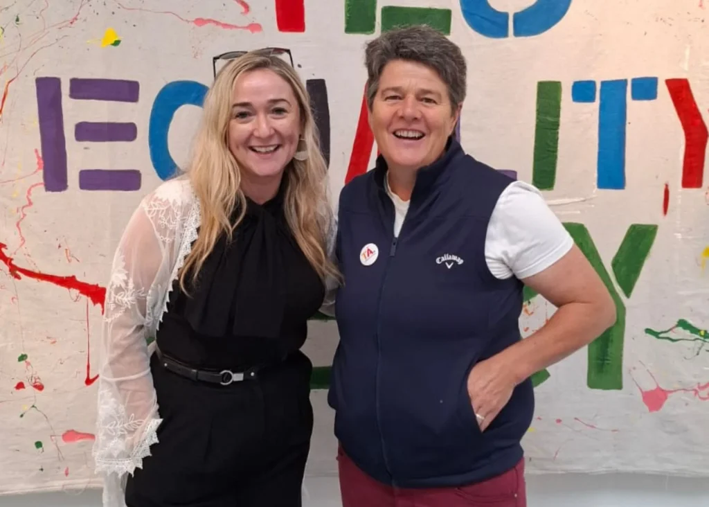 Two smiling women stand before a colorful "EQUALITY" banner at Siamsa Tíre theatre Tralee.