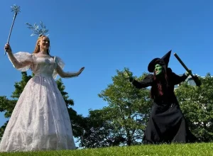 Two women as fairy and witch stand on grass at Siamsa Tíre theatre Tralee under a blue sky.