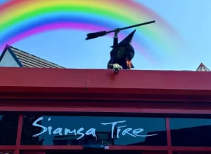 Witch with green face and broom on a roof over "Siamsa Tíre theatre Tralee" under a rainbow.