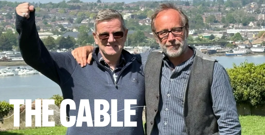 Two men smile arm in arm outdoors, "THE CABLE" text shows; Arts centre Tralee Kerry featured.