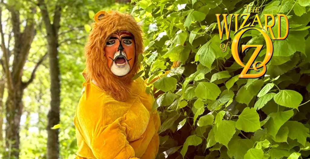 Person in a lion costume by green leaves at The Wizard of Oz, Arts centre Tralee Kerry.