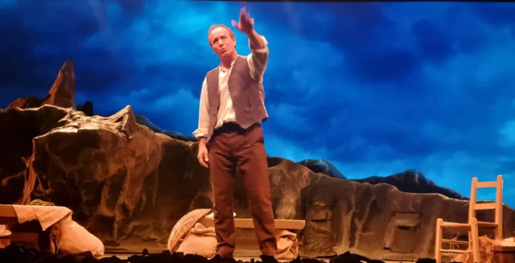 A man in period clothing performs onstage at Siamsa Tíre theatre Tralee under blue lighting.