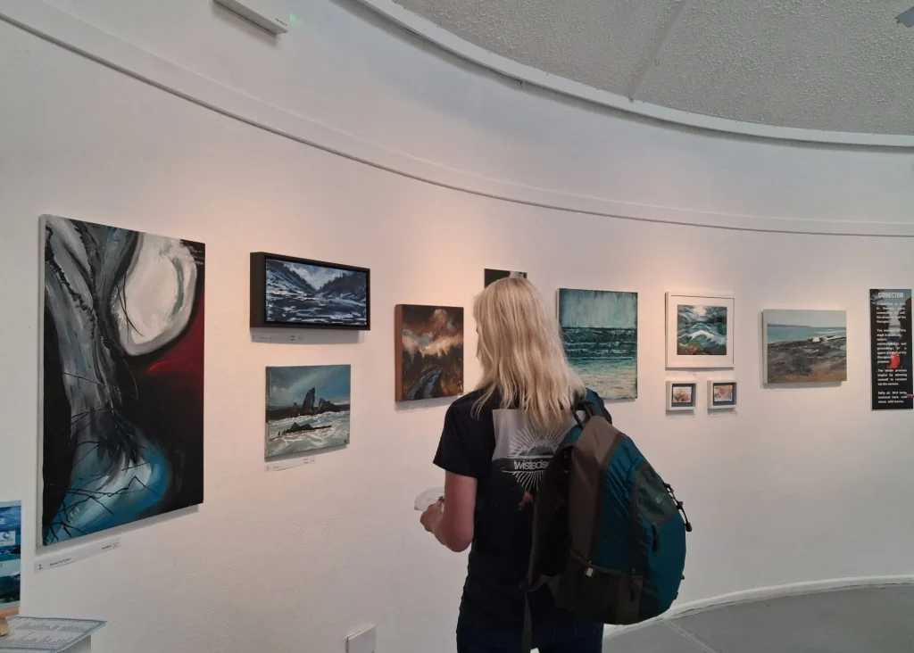 Person with a backpack views ocean art at the Arts Centre Tralee Kerry’s curved, white-walled gallery.