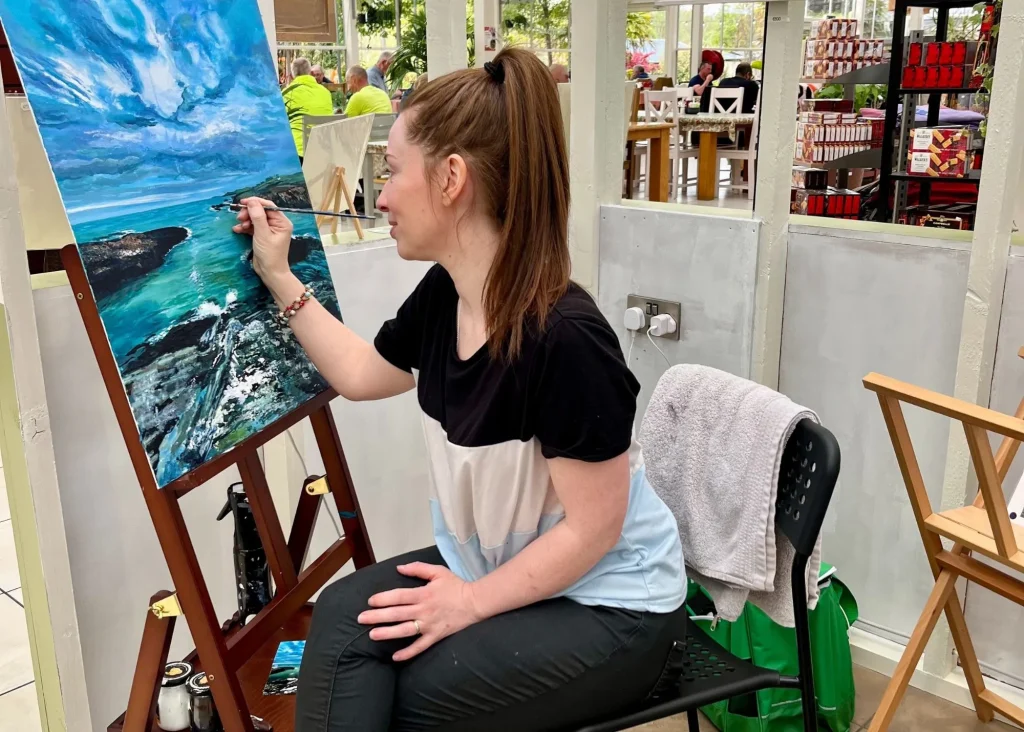 Woman painting a seascape, inspired by Siamsa Tíre traditional Irish arts performances.