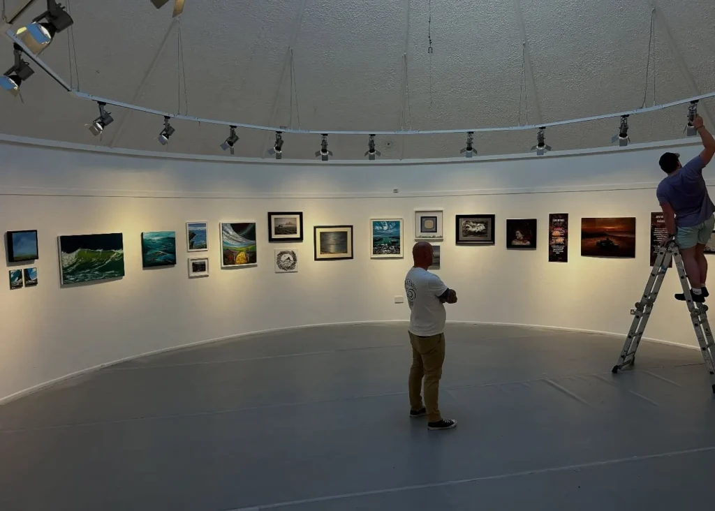 Two people hang art at Siamsa Tíre theatre Tralee; one arranges frames from a ladder.