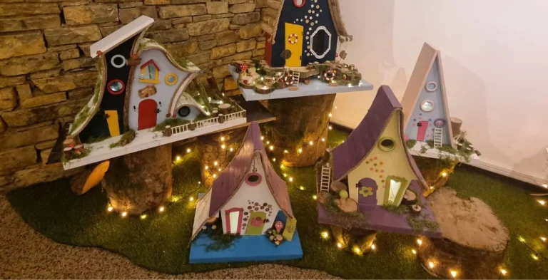 Five colorful fairy houses on logs, like scenes from a Siamsa Tíre traditional Irish arts performance.