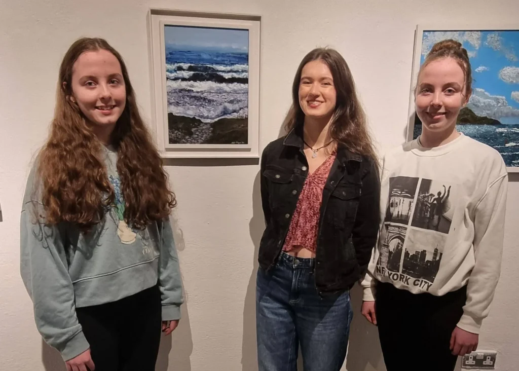 Photo of 3 young girls standing in front of two paintings hanging on a wall