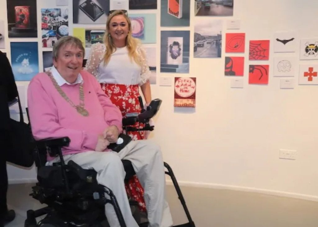 A blonde woman standing beside a man in a wheelchair