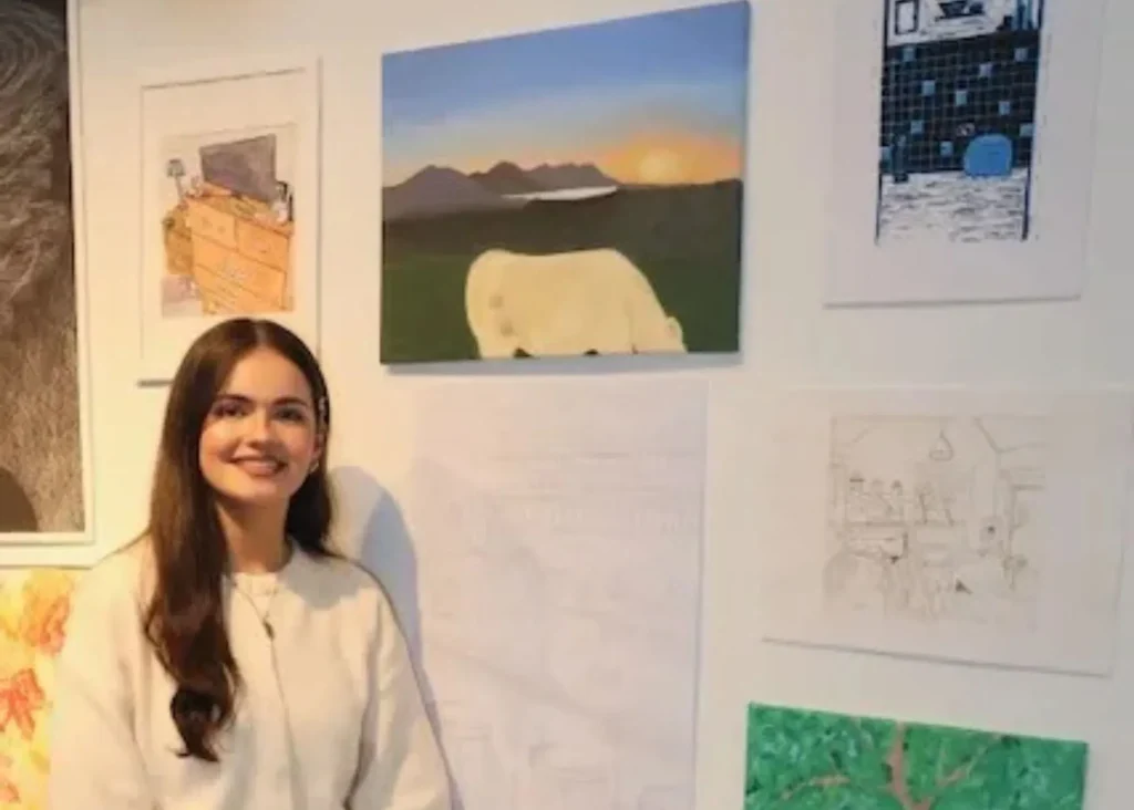 A young woman standing beside a painting on a wall