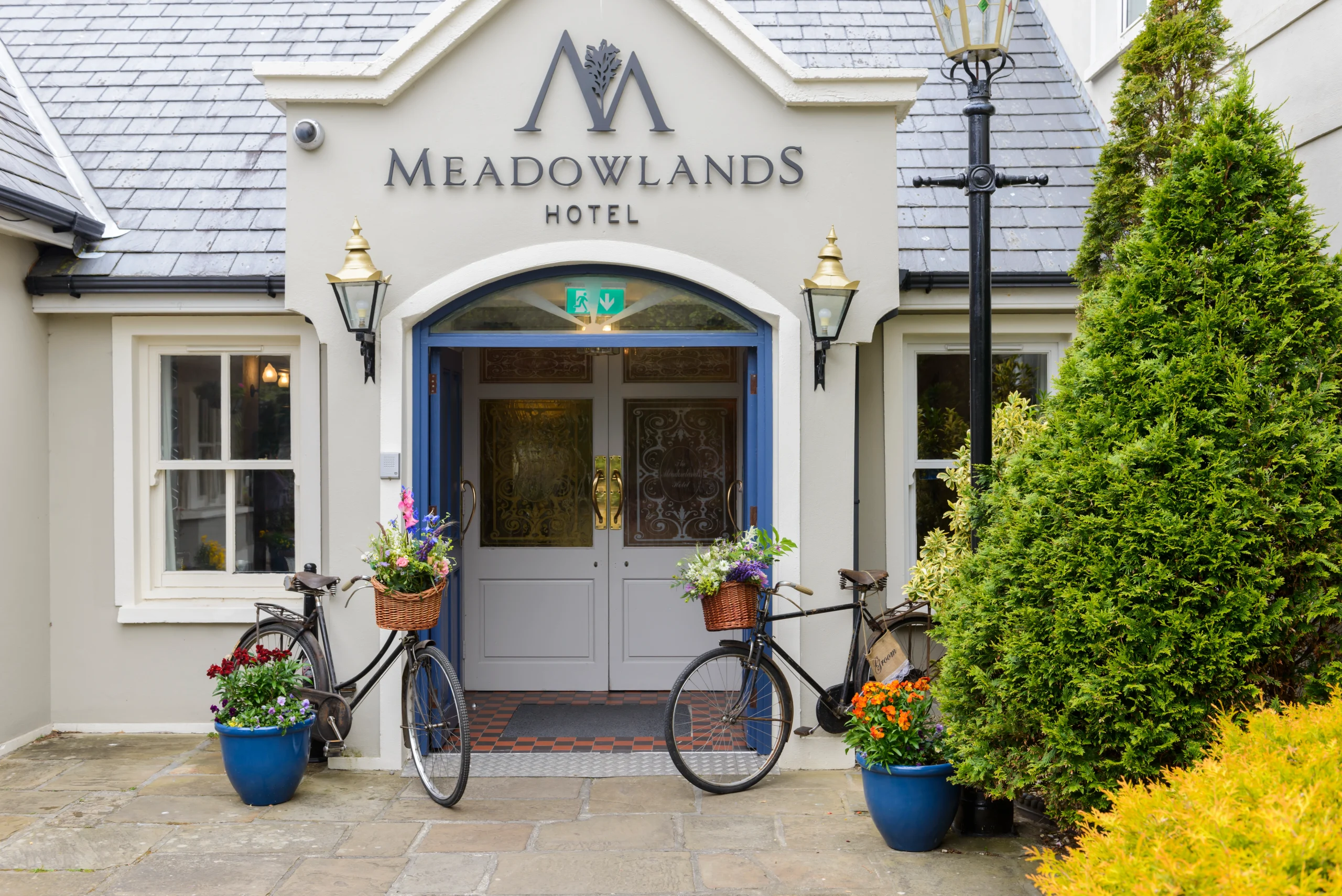 Photo of exterior front door of a hotel, sign above it reads 'Meadowlands Hotel'