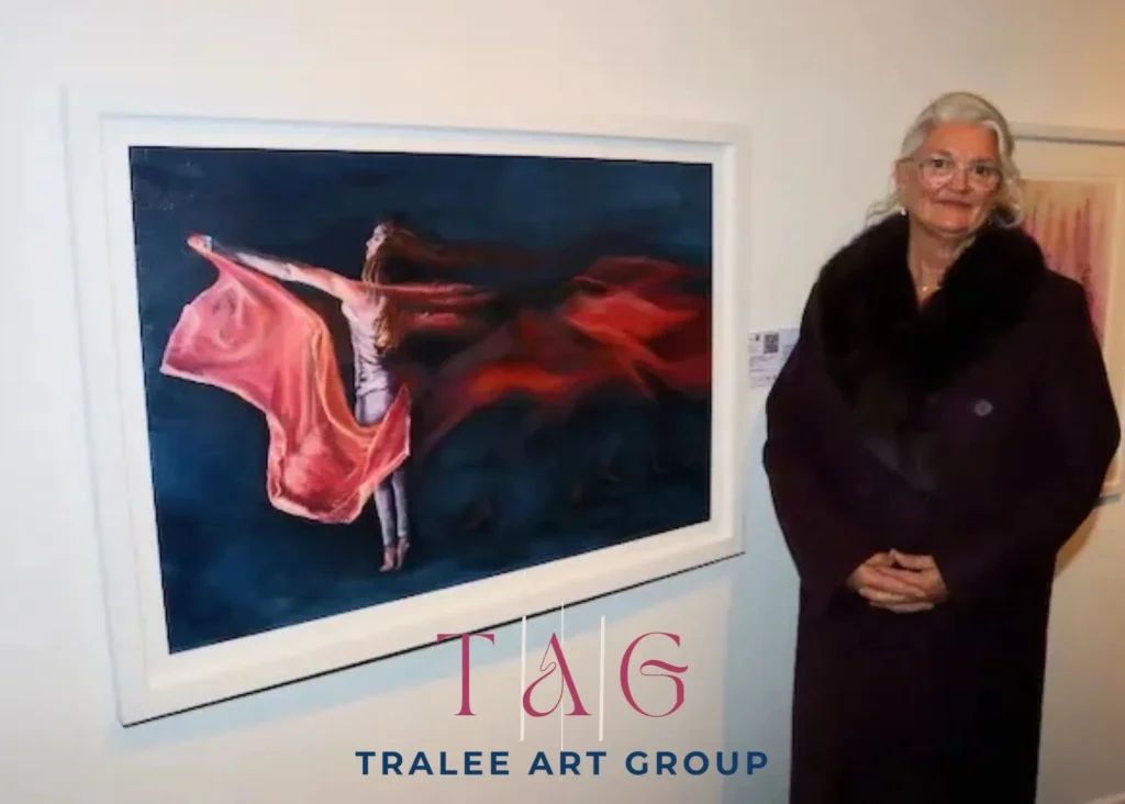 ***Photo of a lady standing next to a painting on a wall. Logo Text "Tralee Art Group"