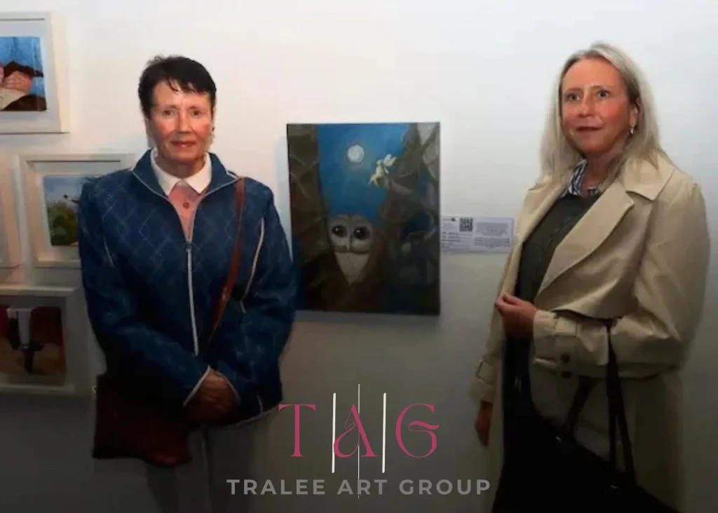 ***Photo of two ladies either side of a painting of an owl.Logo Text "Tralee Art Grop"